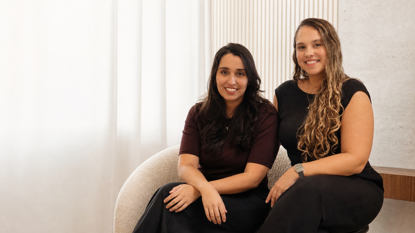 Isis Barbosa e Anna Botsis em um retrato profissional, sentadas em um ambiente contemporâneo da IBA Arquitetura.